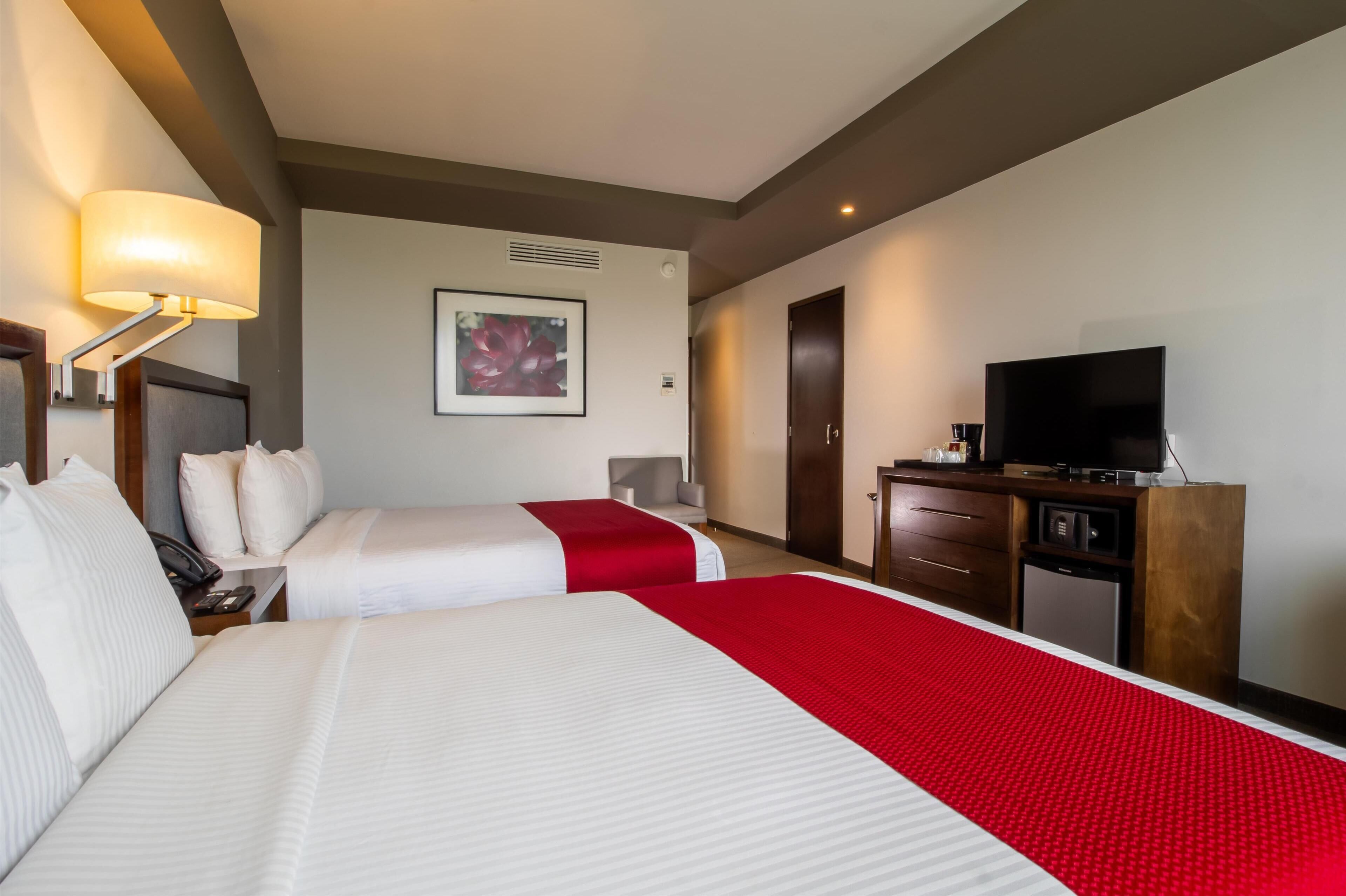 Une chambre d’hôtel avec deux lits, une télévision, un bureau et un mur d’accent de couleur rouge.