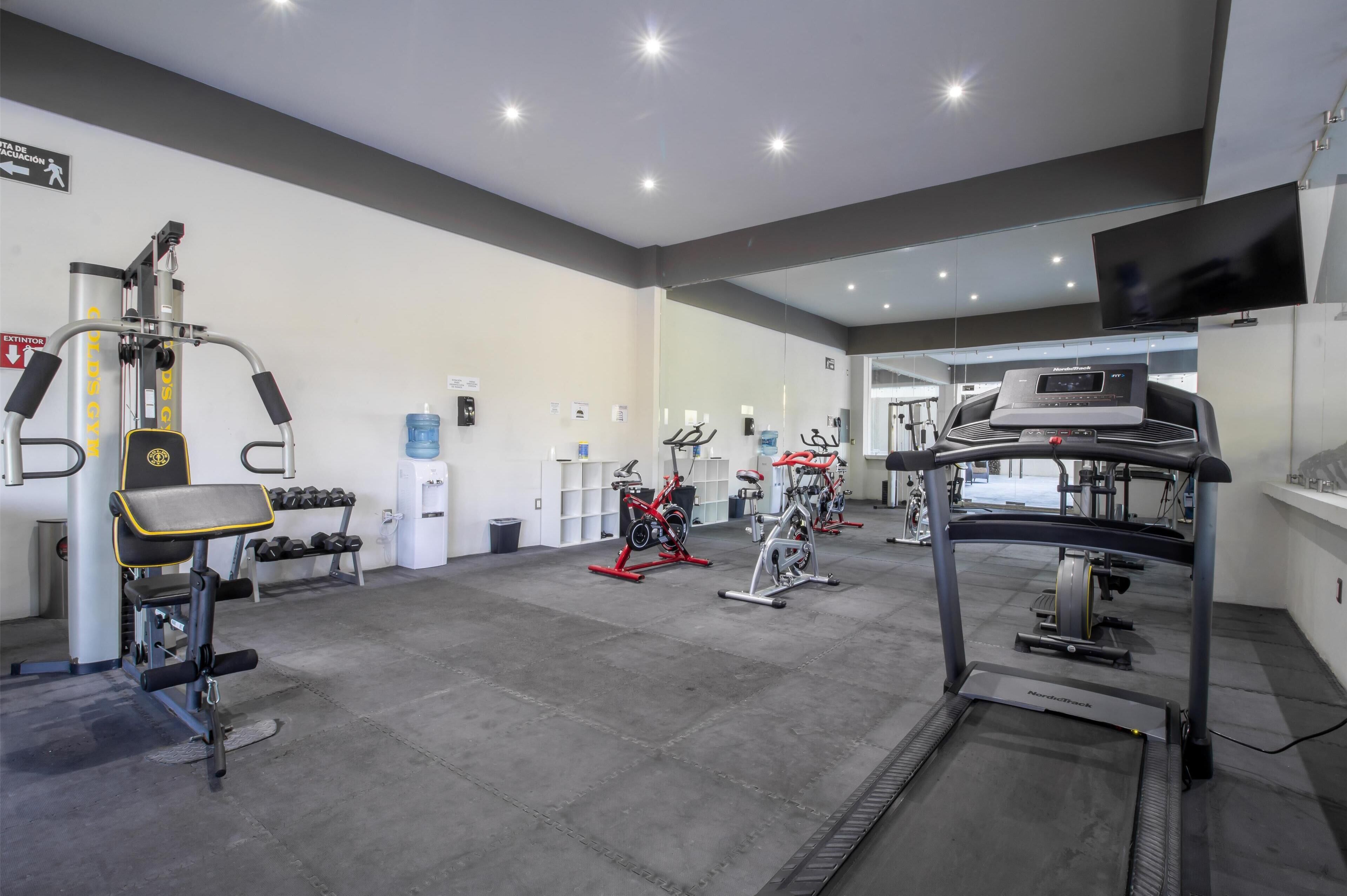 Une salle de sport moderne équipée de machines de cardio, d’appareils de musculation et d’haltères.