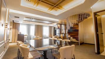 A spacious conference room with a large table and comfortable chairs, a modern staircase, and a well-lit ceiling with recessed lighting.