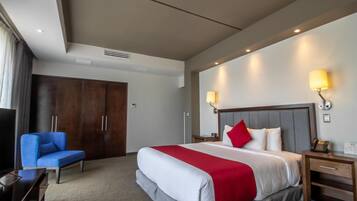 Una habitación de hotel con una cama grande, una silla azul, un armario de madera y dos lámparas de noche.