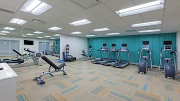 A gym with various exercise equipment, a mirrored wall, and a patterned carpet.