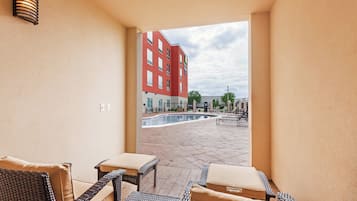 A hotel room with a view of an outdoor swimming pool and a red building in the background.