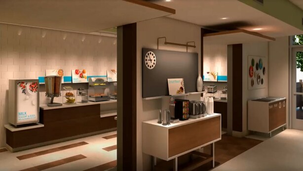 Un espace moderne dédié au petit-déjeuner, équipé d’un distributeur de lait, d’un présentoir de fruits et d’une horloge murale.