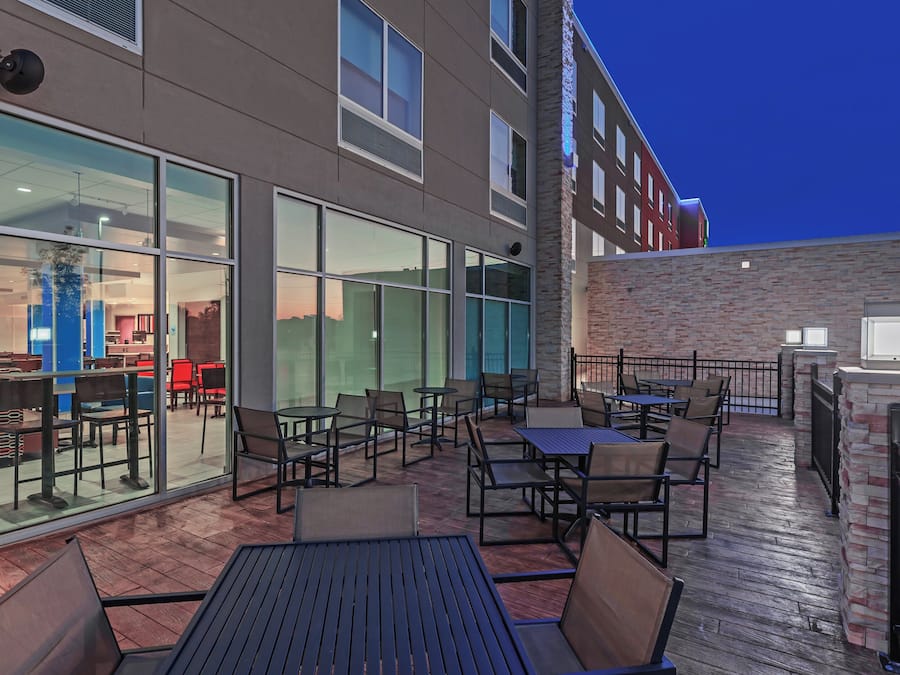 An outdoor patio with tables and chairs, a glass wall, and a brick wall.