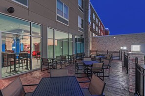 Une terrasse extérieure avec des tables et des chaises, un mur de verre et un mur en briques.