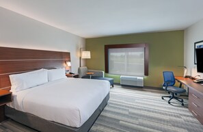 Ein Hotelzimmer mit einem großen Bett, einem Schreibtisch mit Stuhl, einem kleinen Tisch und einem Fenster mit Jalousien.