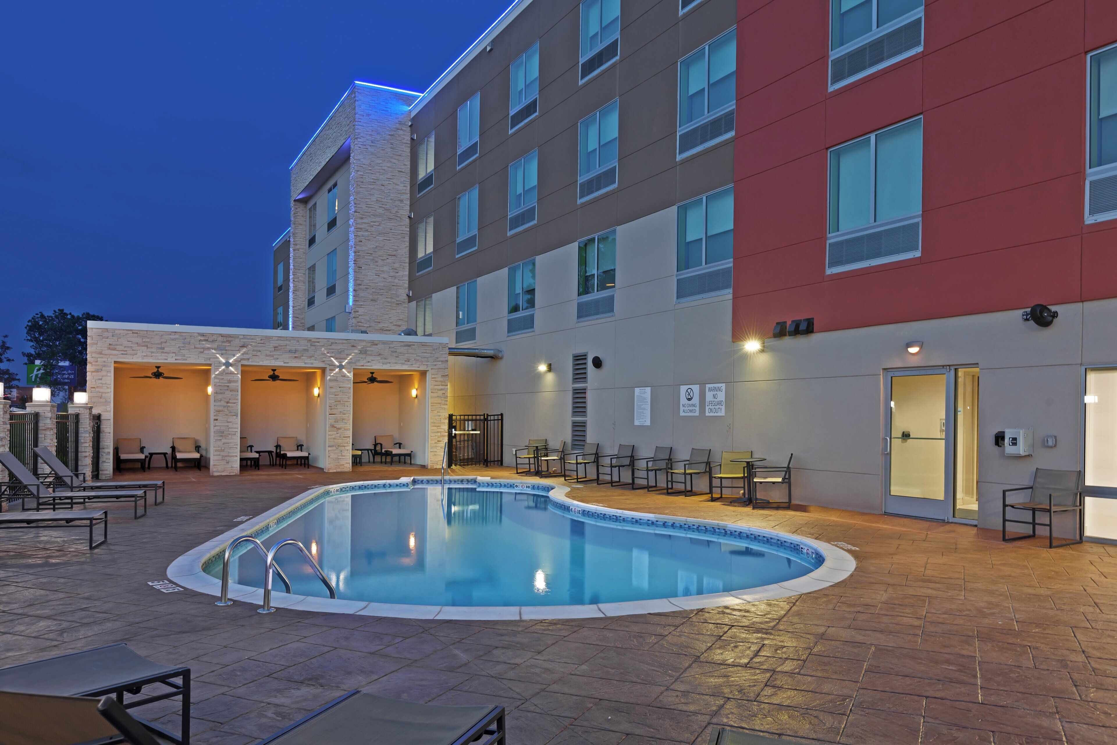 A hotel pool area with a pool, lounge chairs, and a covered seating area.