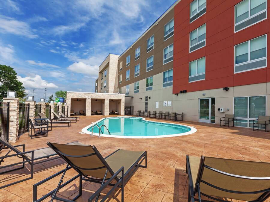 Zona de piscina de hotel con sillones reclinables y un edificio con amplias ventanas.