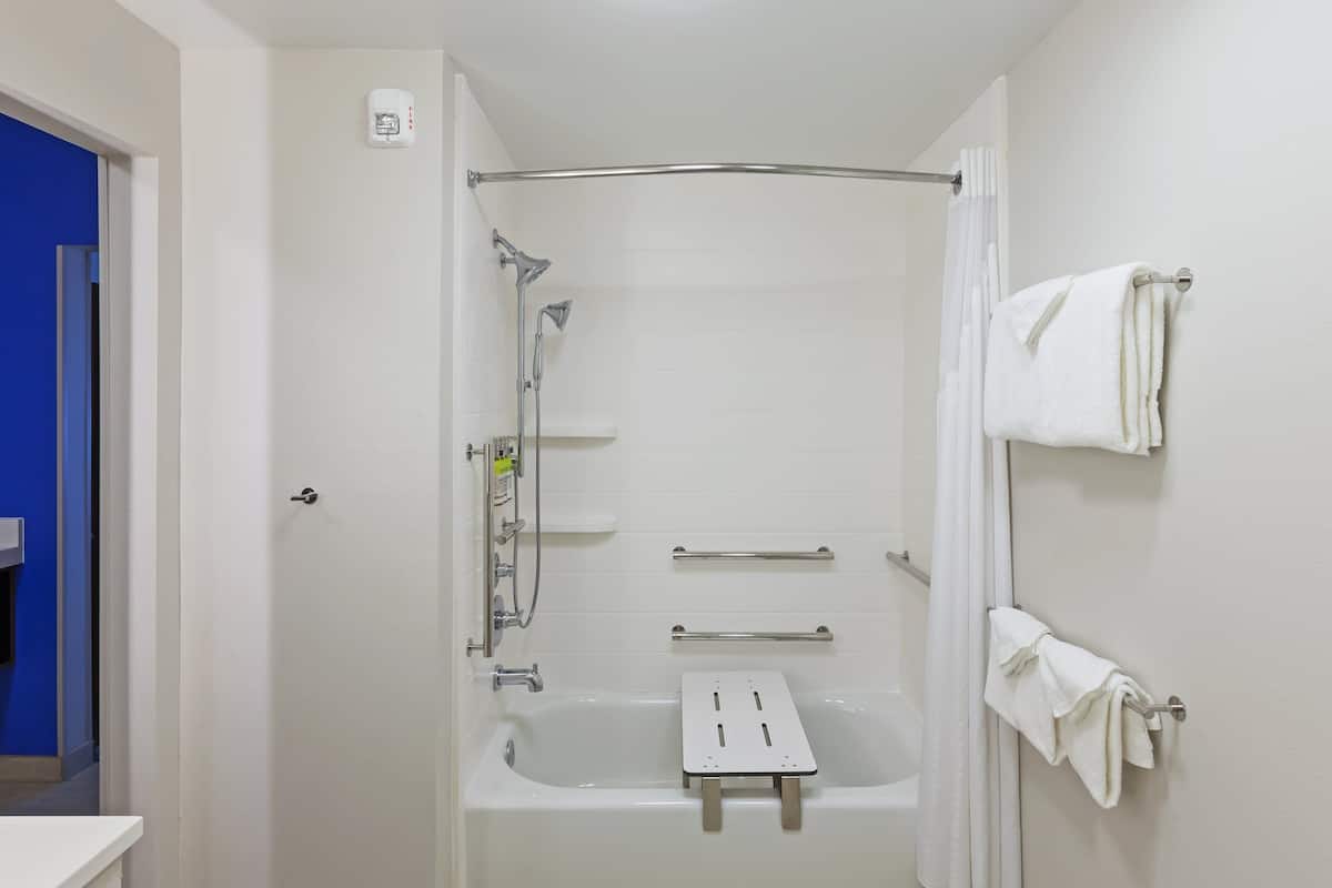 Une salle de bain moderne dotée d’une douche à l’italienne, de barres d’appui, d’un pommeau de douche amovible et d’un porte-serviettes.