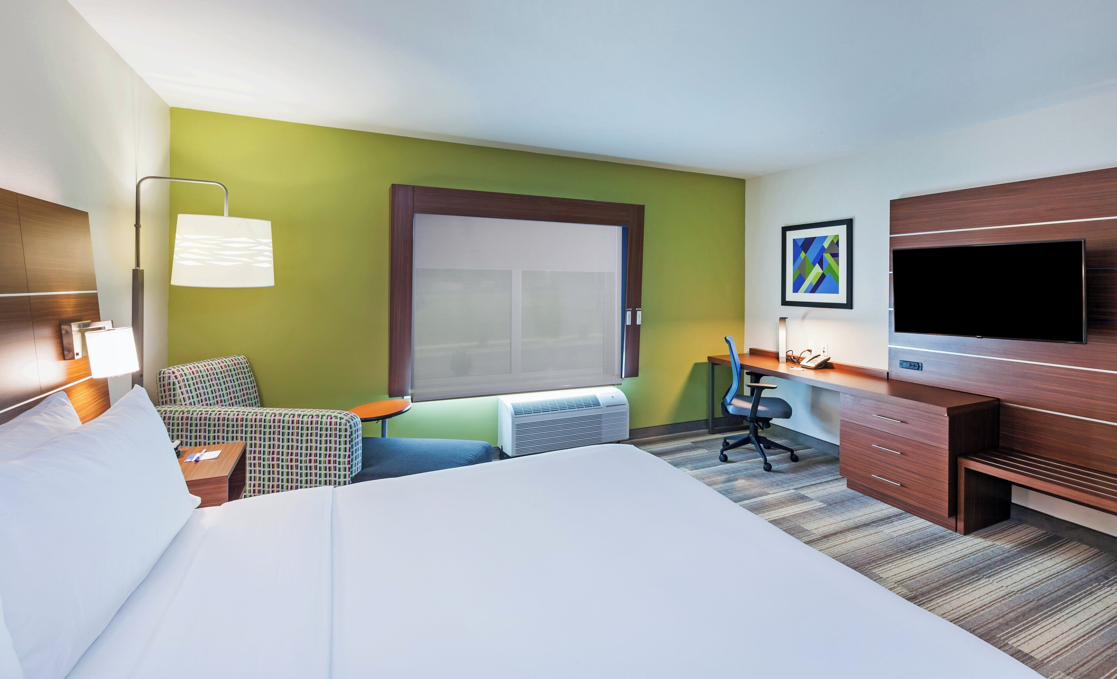 Habitación de hotel con cama, escritorio, silla, televisor y ventana con persianas.