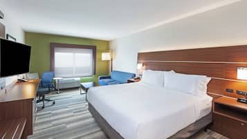 A hotel room with a large bed, a desk with a computer, a chair, a sofa, and a TV.