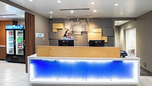 Un comptoir d’accueil doté d’un panneau bleu rétroéclairé, d’un écran numérique et d’une enseigne indiquant « Hollysyn Express & Suites ».