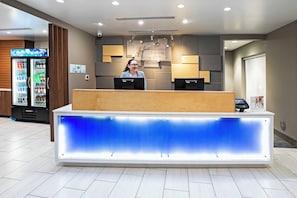 Un comptoir d’accueil doté d’un panneau bleu rétroéclairé, d’un écran numérique et d’une enseigne indiquant « Hollysyn Express & Suites ».