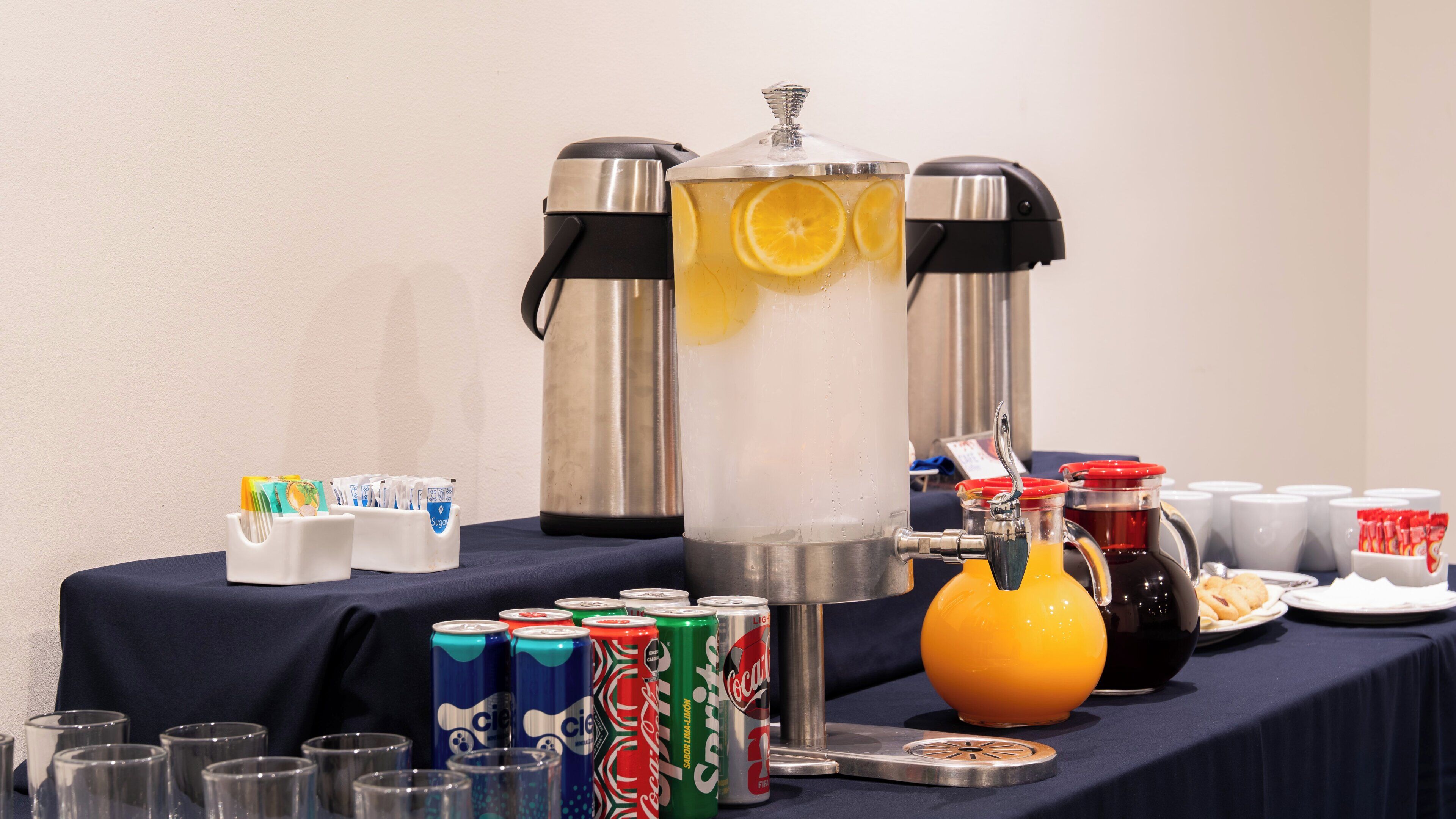 Un espace dédié aux boissons, équipé d’un grand distributeur, de gobelets et de diverses canettes de boissons.