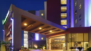 Una entrada de hotel con un corredor cubierto, una zona de recepción y una fachada de edificio moderna.