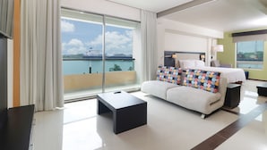 A modern hotel room with a large balcony, a bed, a sofa, and a coffee table.