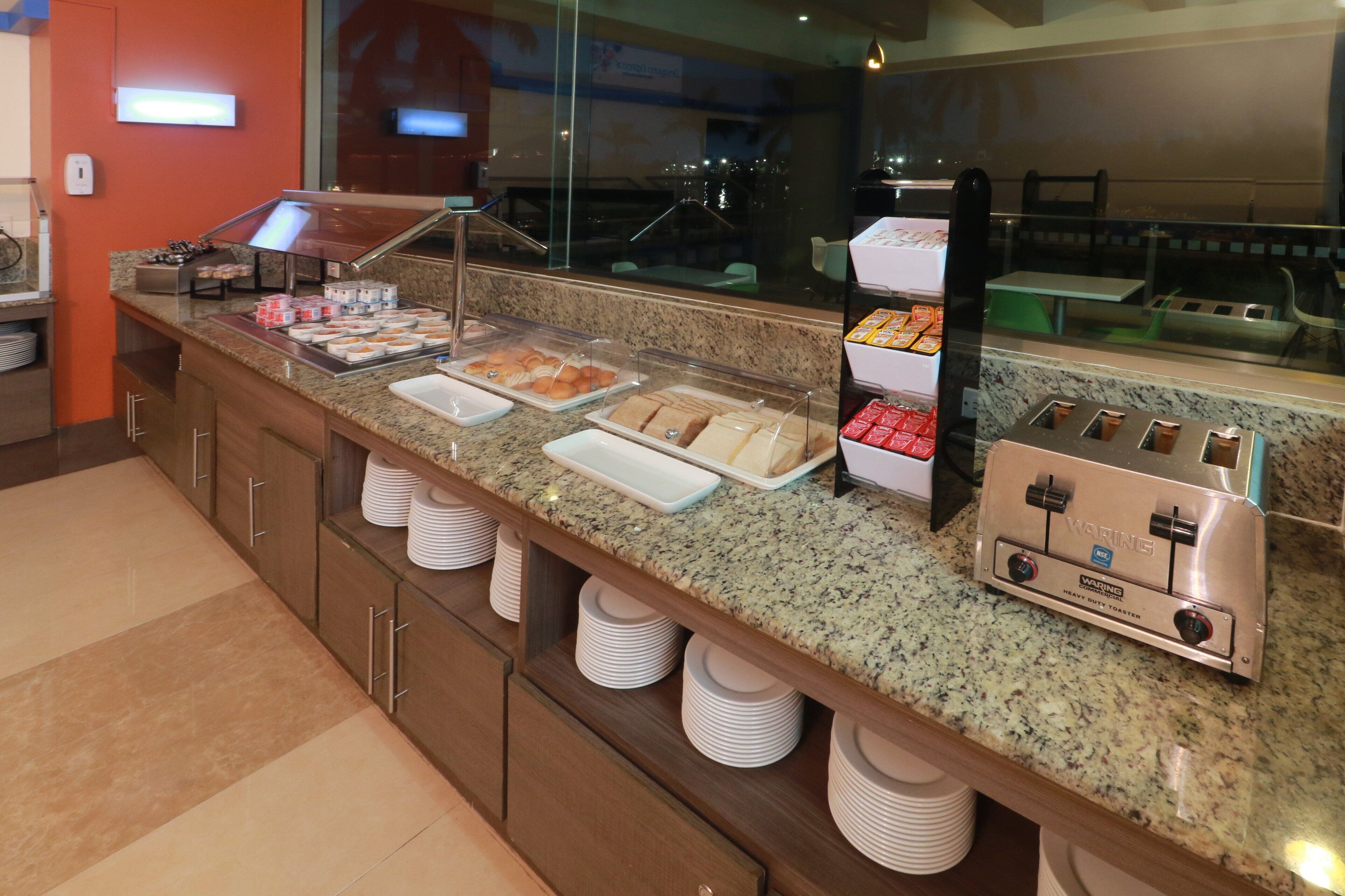 A buffet counter with various food items, a coffee machine, and stacked plates.