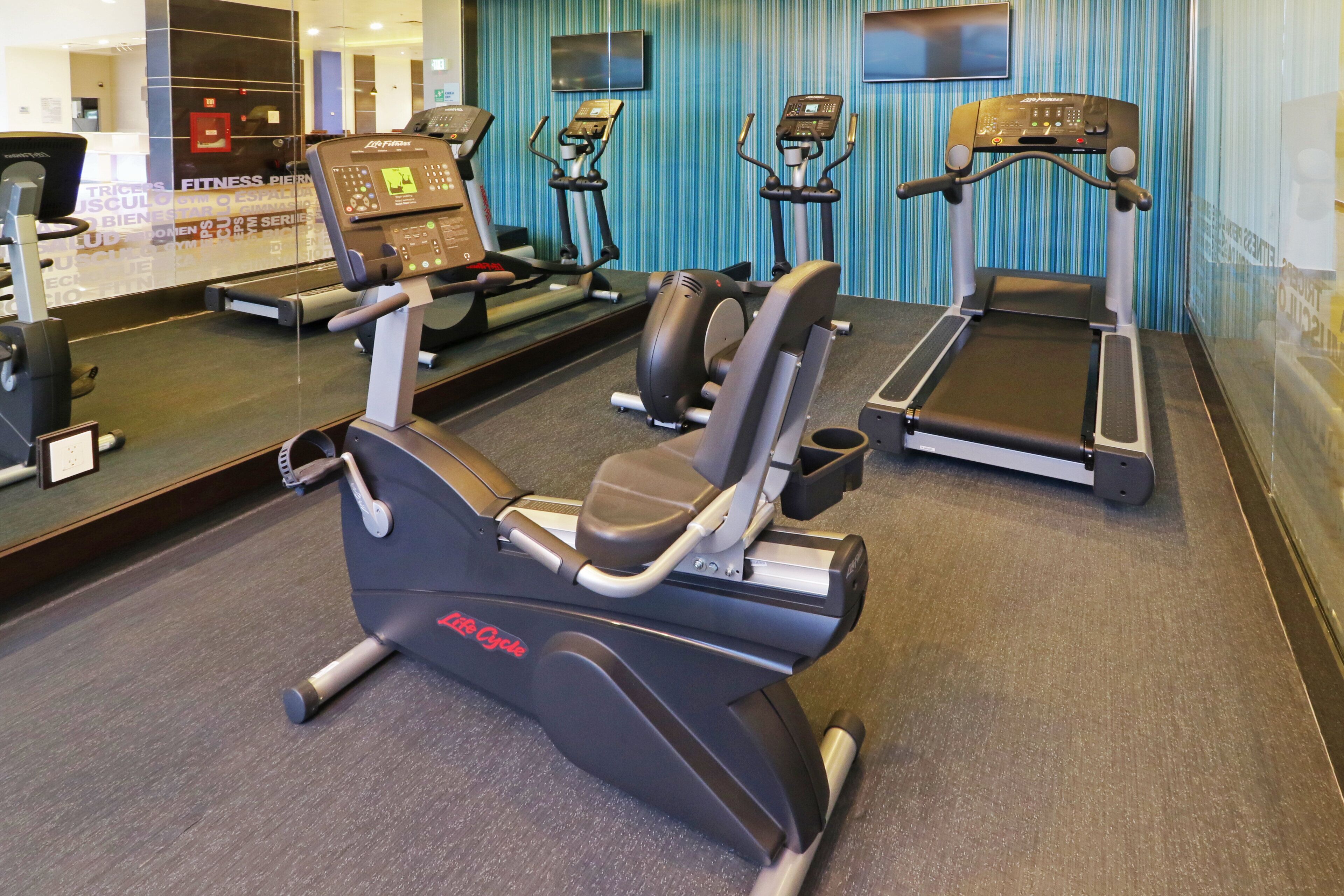 Un gimnasio con diversos equipos de ejercicio, incluyendo cintas de correr, una máquina elíptica y una bicicleta estática.