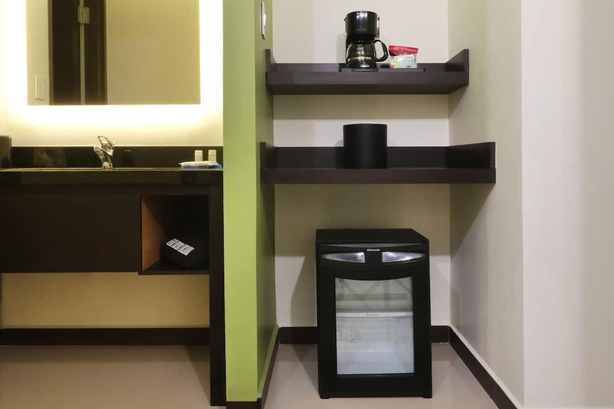 Uma casa de banho moderna com uma pia, espelho e prateleiras com uma máquina de café e um cesto de lixo.