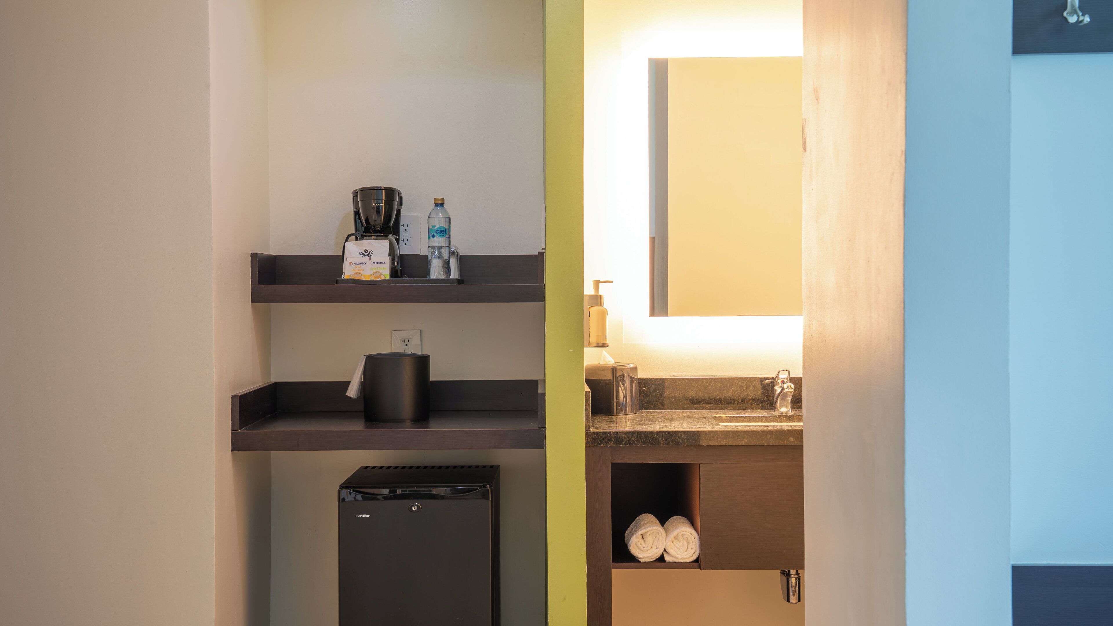 Una kitchenette compacta con cafetera, hervidor y un refrigerador pequeño.