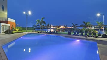 Una piscina con sillas de descanso y un edificio al fondo.