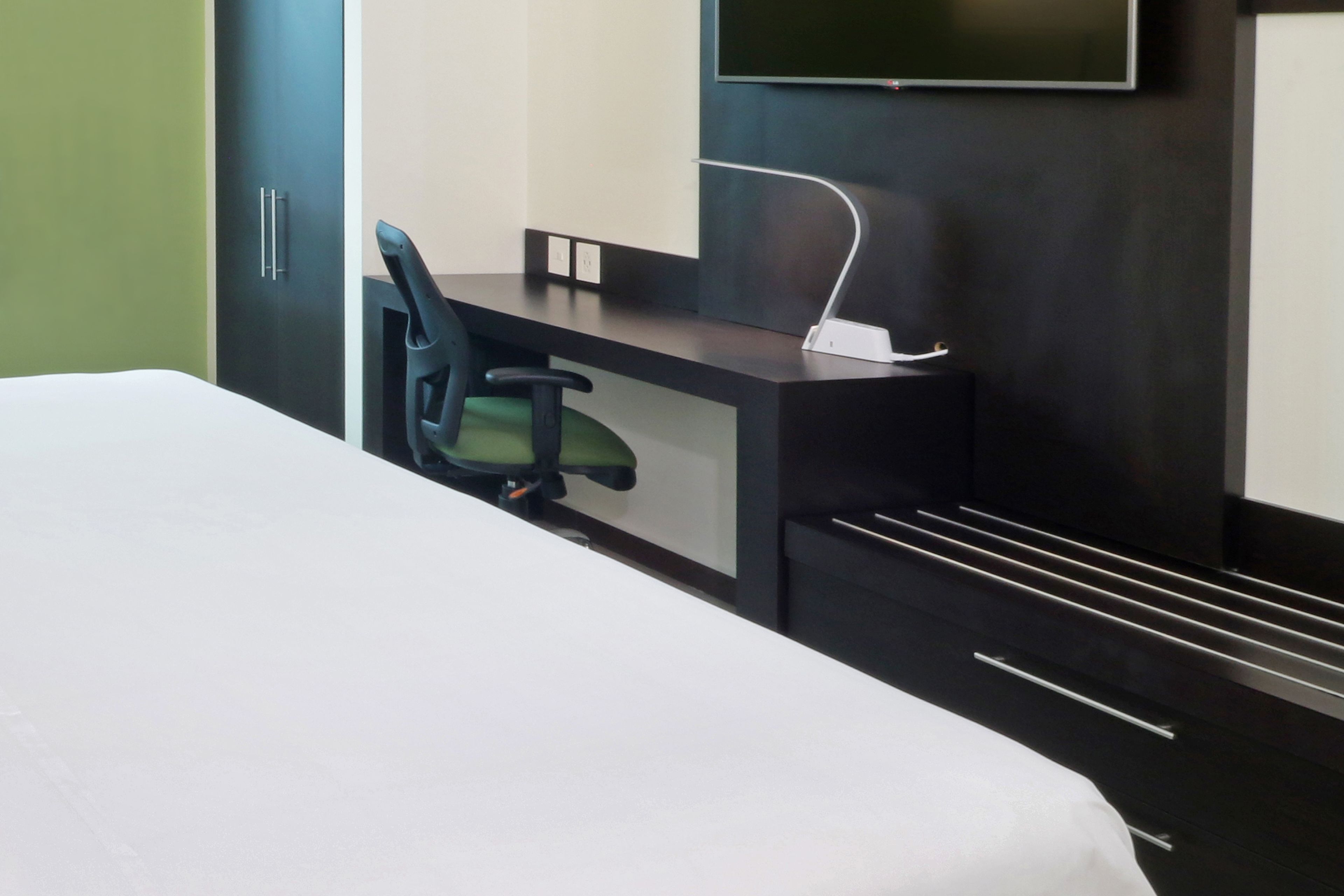 A hotel room with a bed, a desk, a chair, and a TV mounted on the wall.