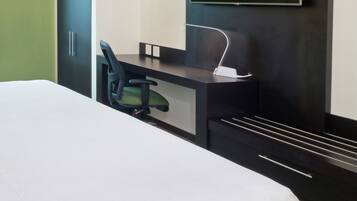 A hotel room with a bed, a desk, a chair, and a TV mounted on the wall.