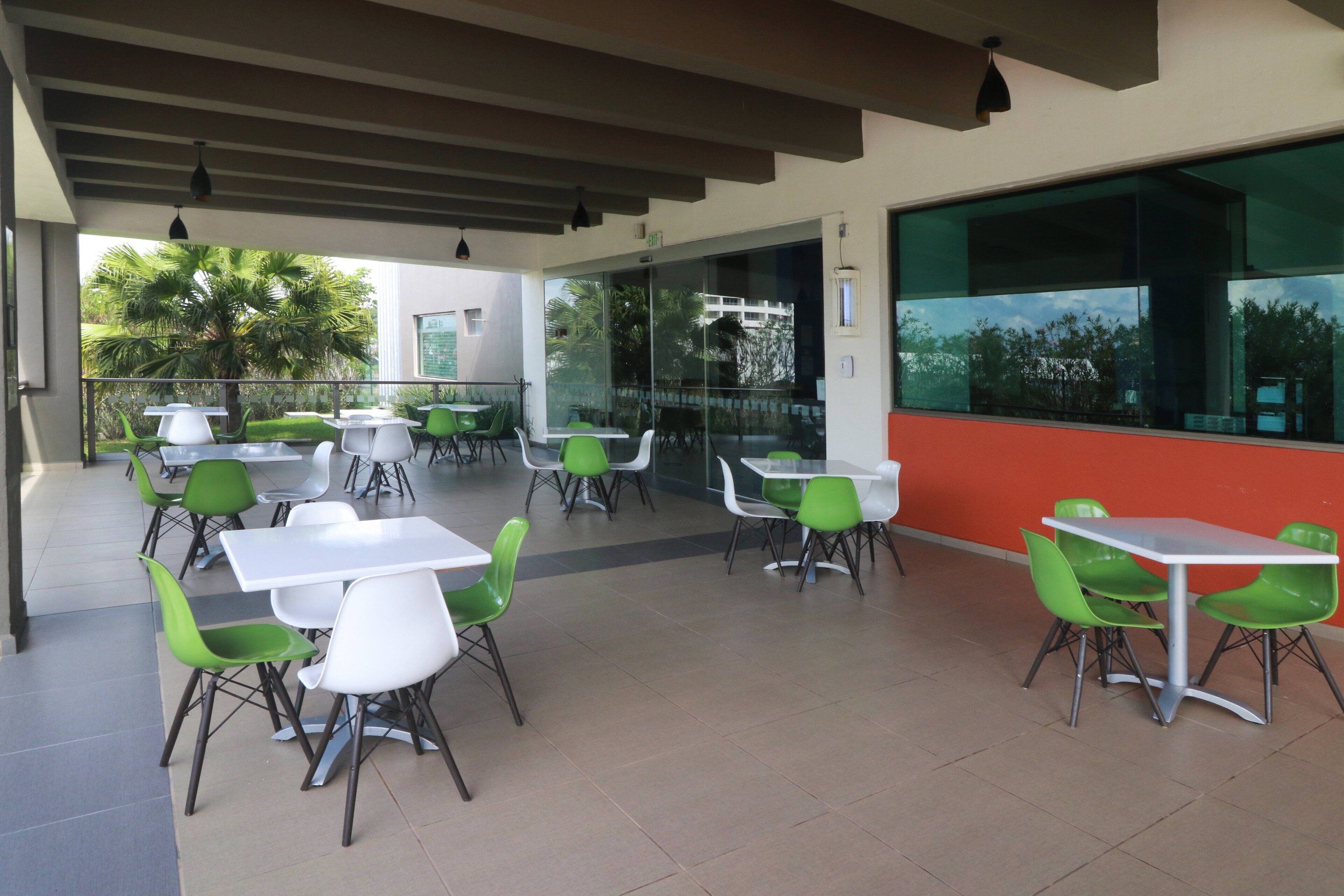 An outdoor cafe area with tables and chairs, large windows, and a view of palm trees.
