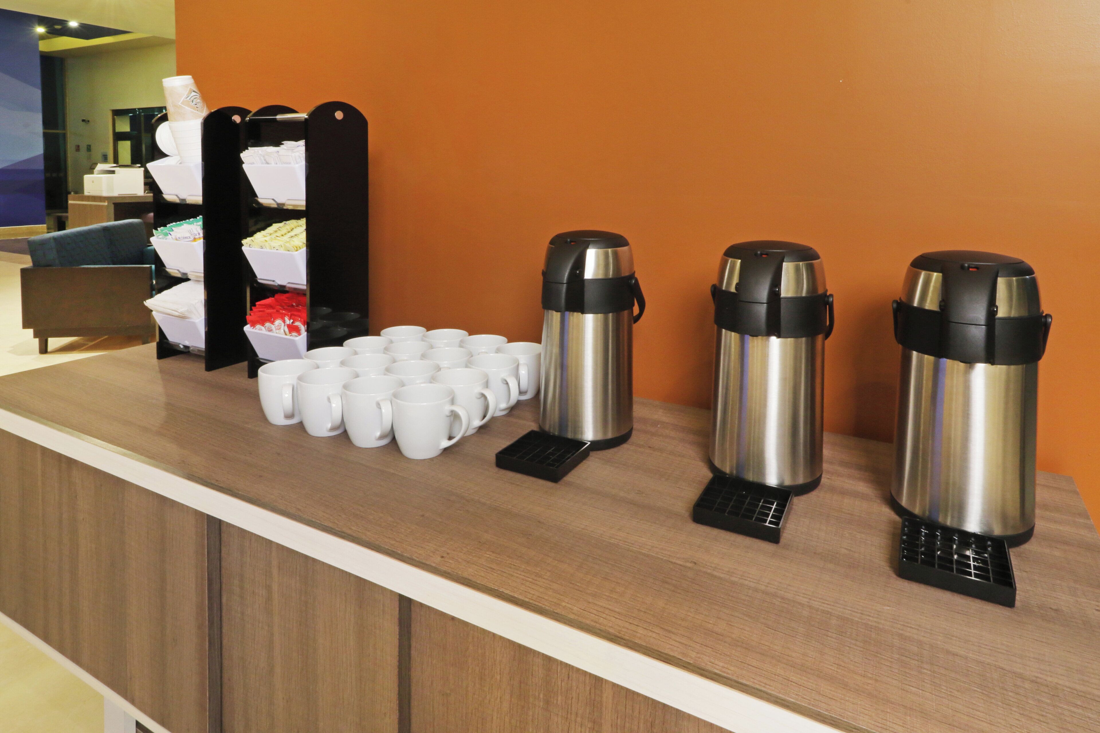 Mostrador con tazas de café y porsiones para hervir agua, señal de una estación de café autoservicio.