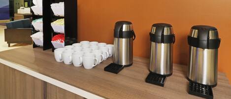 Mostrador con tazas de café y porsiones para hervir agua, señal de una estación de café autoservicio.