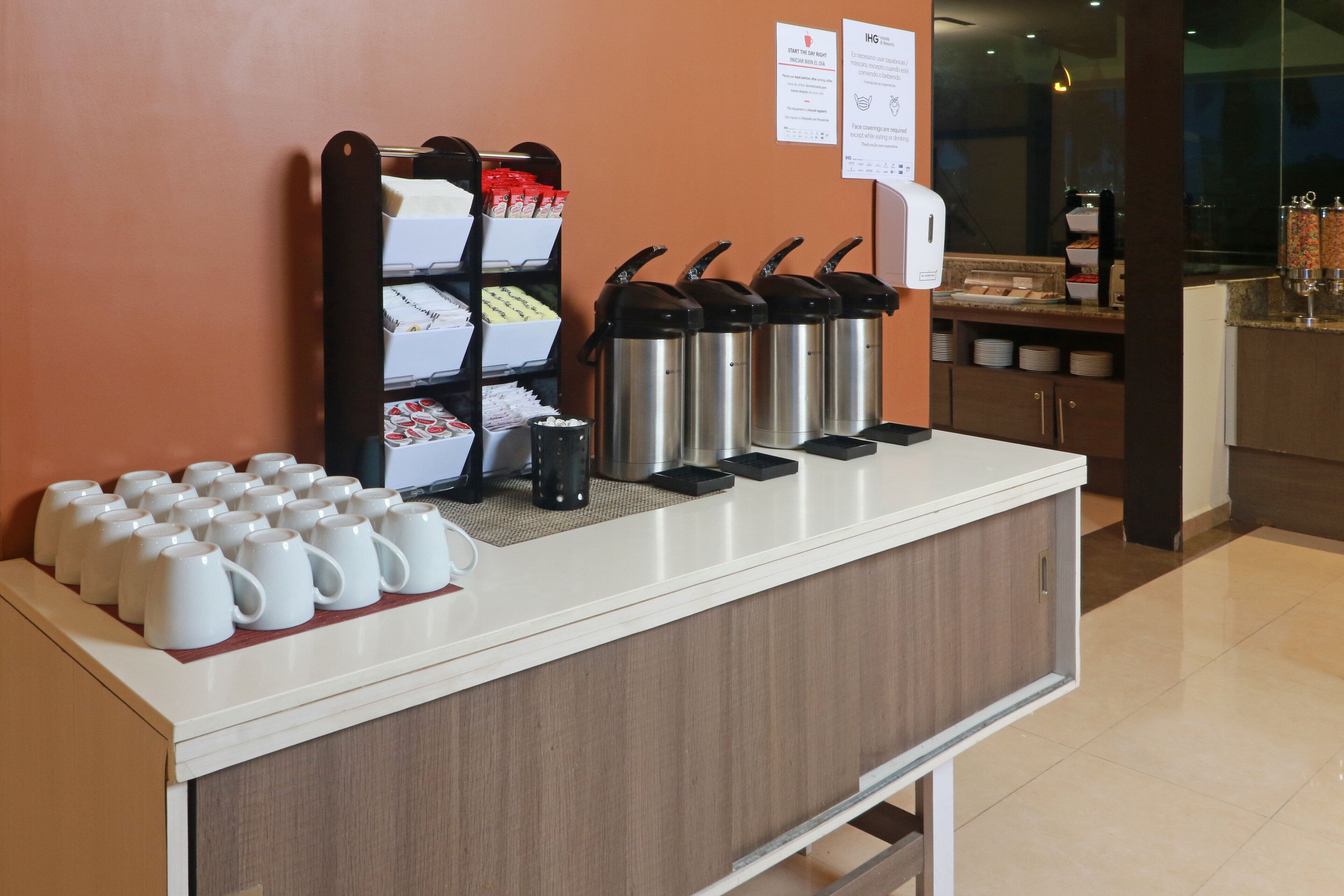 Een ontbijtbalk met koffiezetapparaten, een koffieautomaat en diverse ontbijtartikelen.