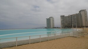 A beach with a swimming pool, a wooden deck, and a sandy area. There are two tall buildings in the background. - Alojamientos La Serena (La Serena)