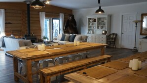 A wooden dining table with benches, a bear sculpture, a fireplace, and a cozy seating area with cushions.
