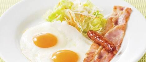 Un plato con dos huevos estrellados, una loncha de tocino y lechuga rallada al lado.