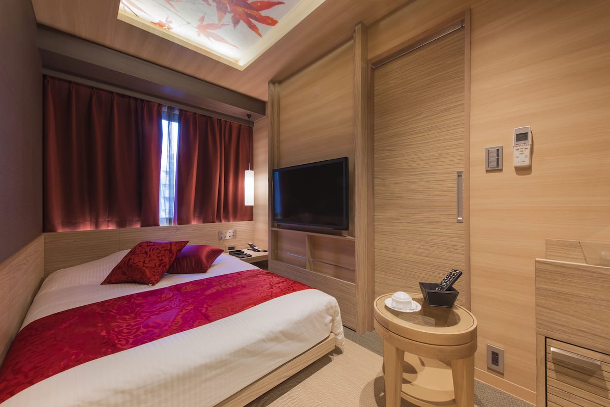 A hotel room with a bed, a television, a bedside table, and a ceiling light.
