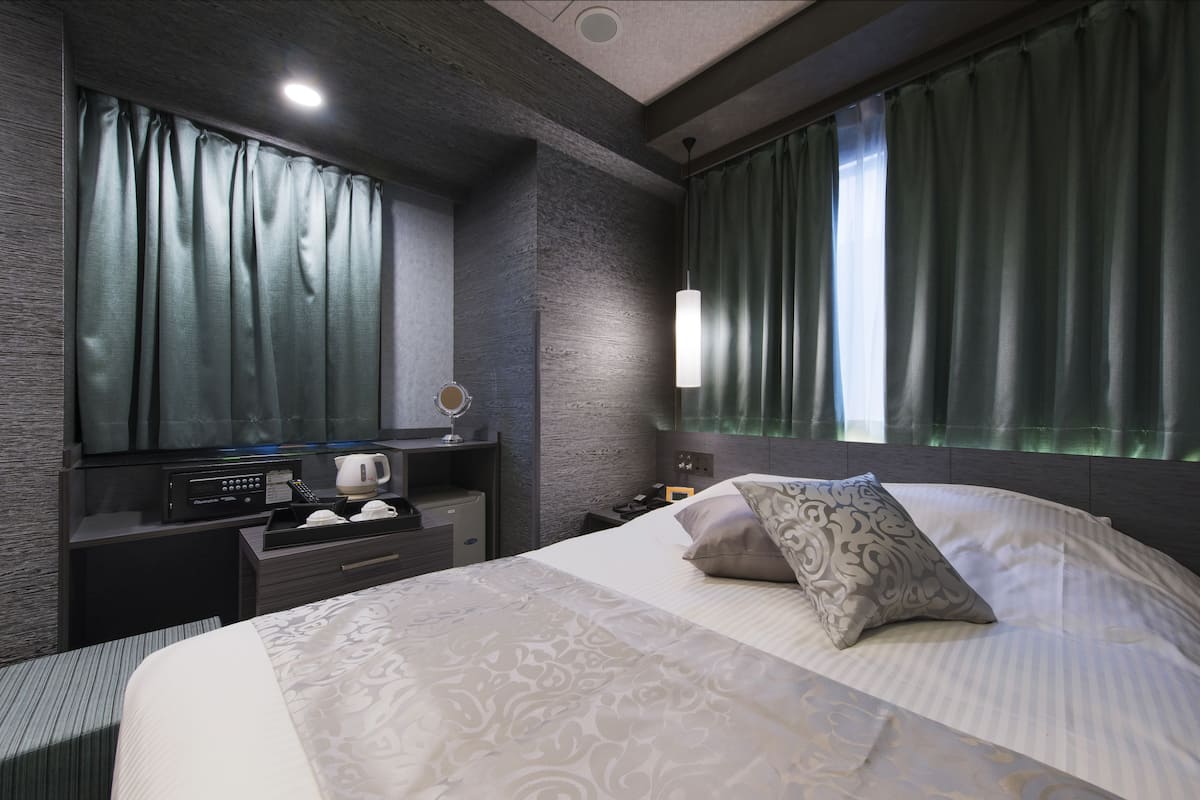 A modern hotel room with a large bed, a bedside table with a lamp, a flat-screen TV, and a coffee machine.