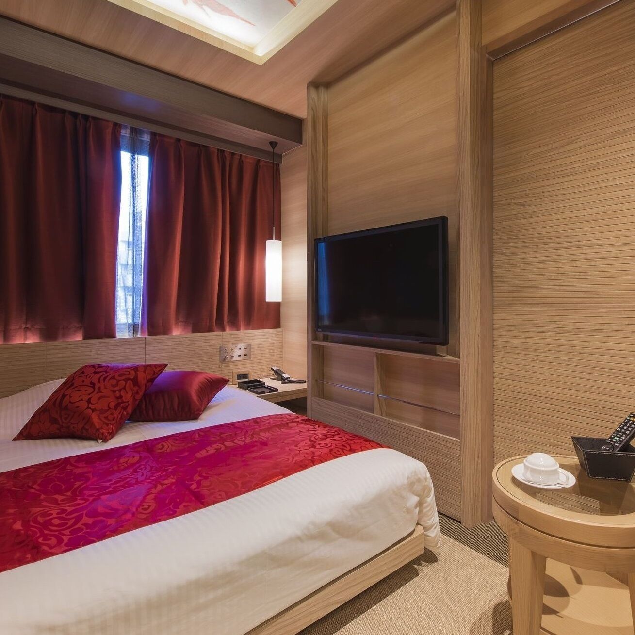 Habitación de hotel con cama, televisor, mesita de noche con una taza y control remoto, y ventana con cortinas.