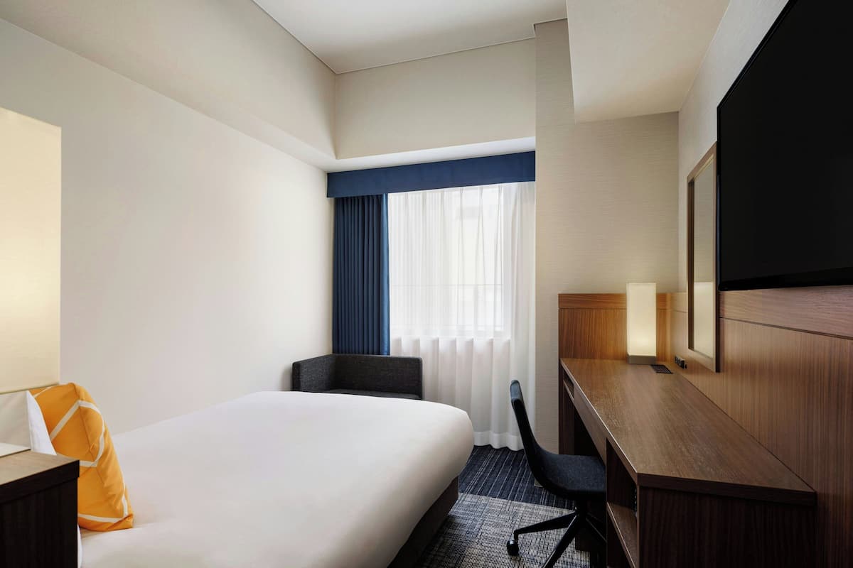 Une chambre d’hôtel avec un grand lit, un bureau, une chaise et un téléviseur.