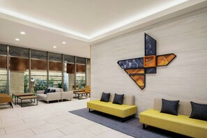 A modern lobby with a yellow sofa, a white sofa, and a brown sofa. There is a large wall art piece and a window with a view of greenery. - Four Points Flex by Sheraton Osaka Shinsaibashi (Osaka)