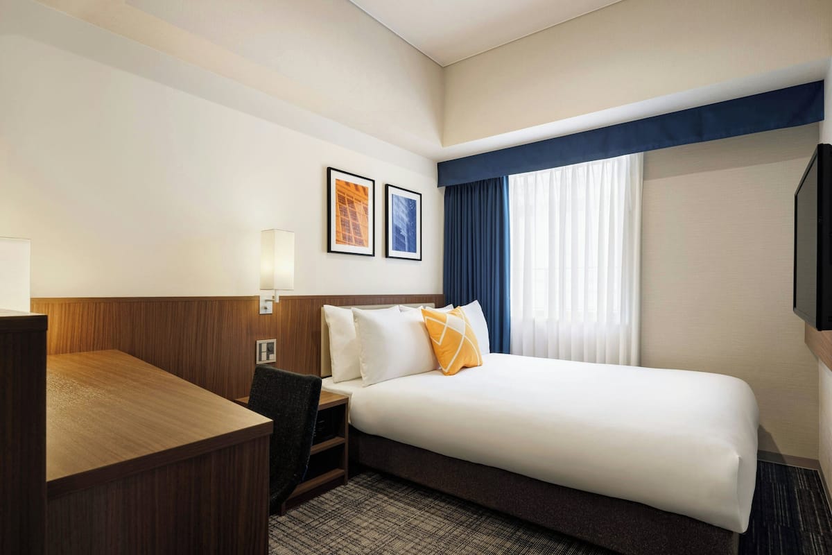 Une chambre d’hôtel avec un lit, un bureau, une chaise et deux tableaux encadrés au mur.