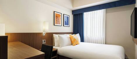A hotel room with a bed, a desk, a chair, and two framed pictures on the wall.