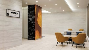 Um interior moderno com parede de mármore, uma placa com a inscrição "OSAKA SHINSAIBASHI" e uma área de estar com sofá e cadeiras.