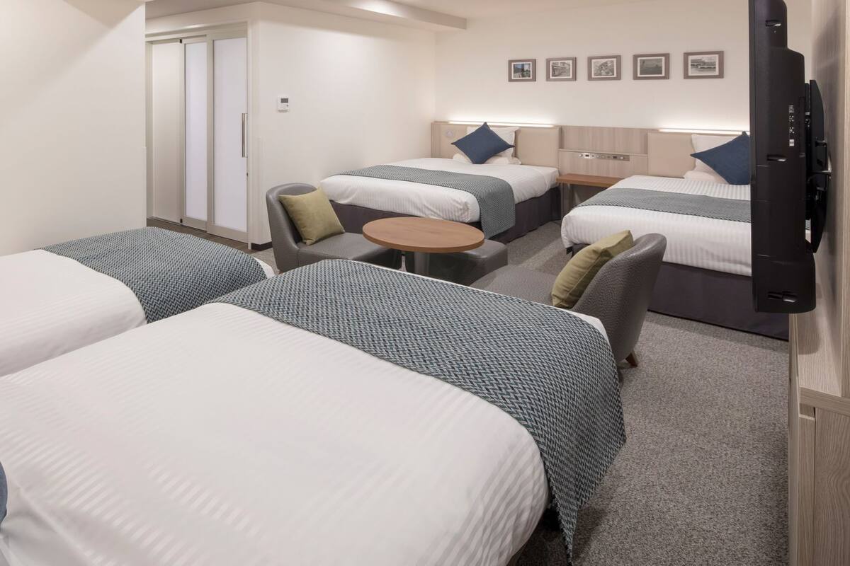 A hotel room with two beds, a small round table, a sofa, and a TV.