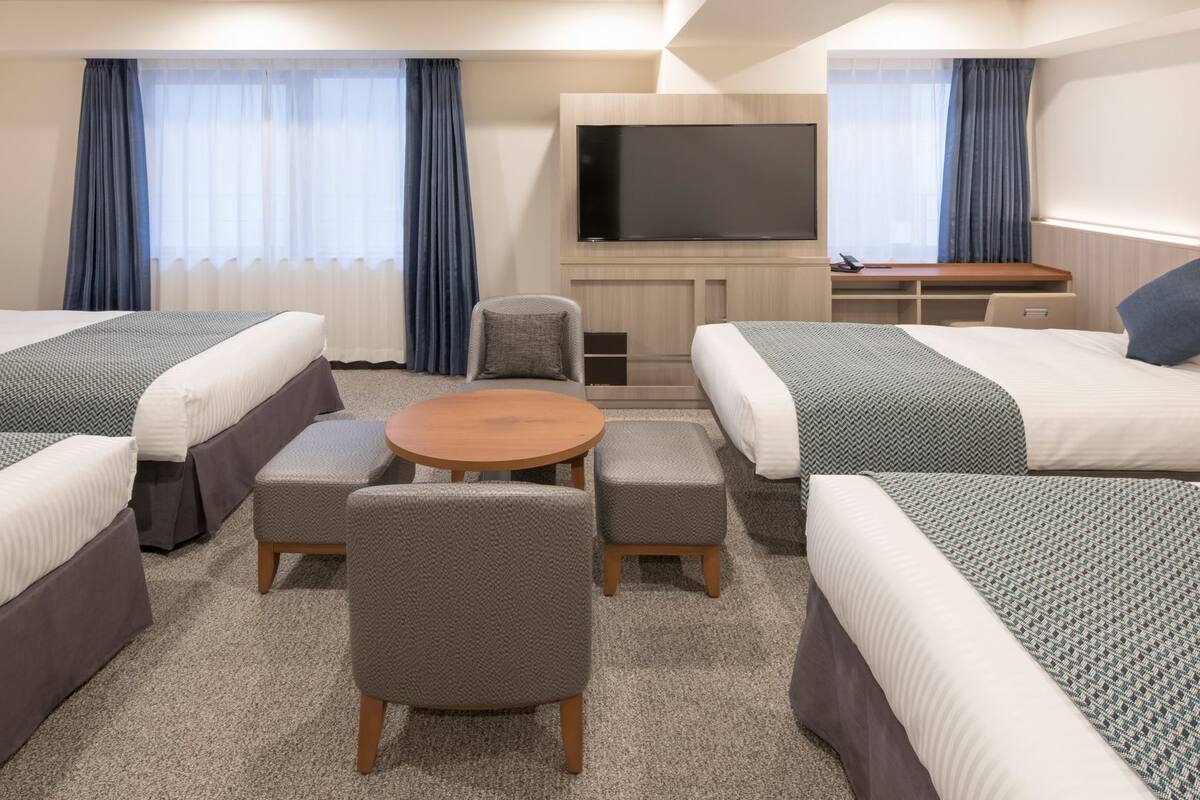 A hotel room with four beds, a TV, a small round table, and a seating area.