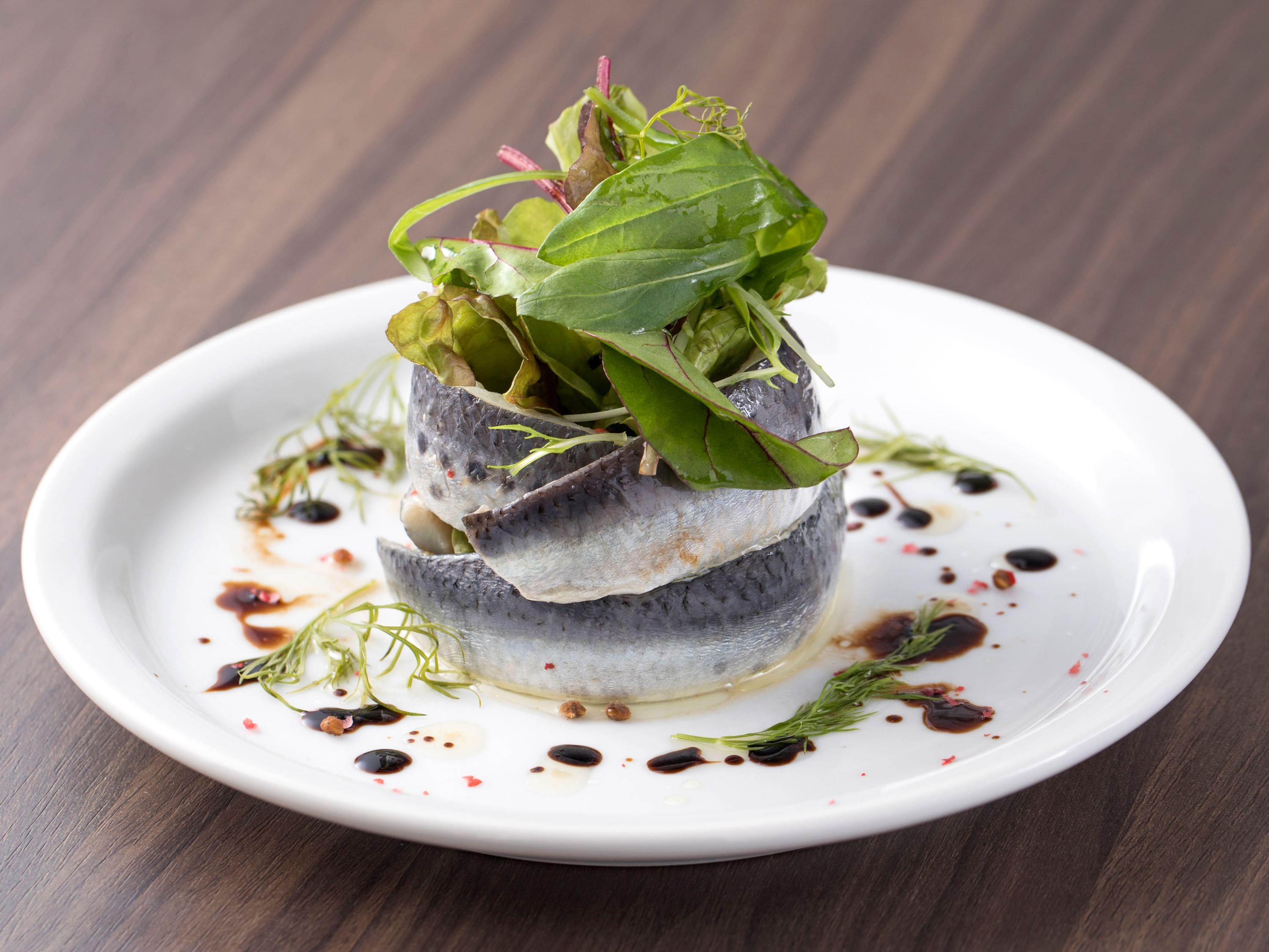 A dish with fish and greens on a white plate with sauce.