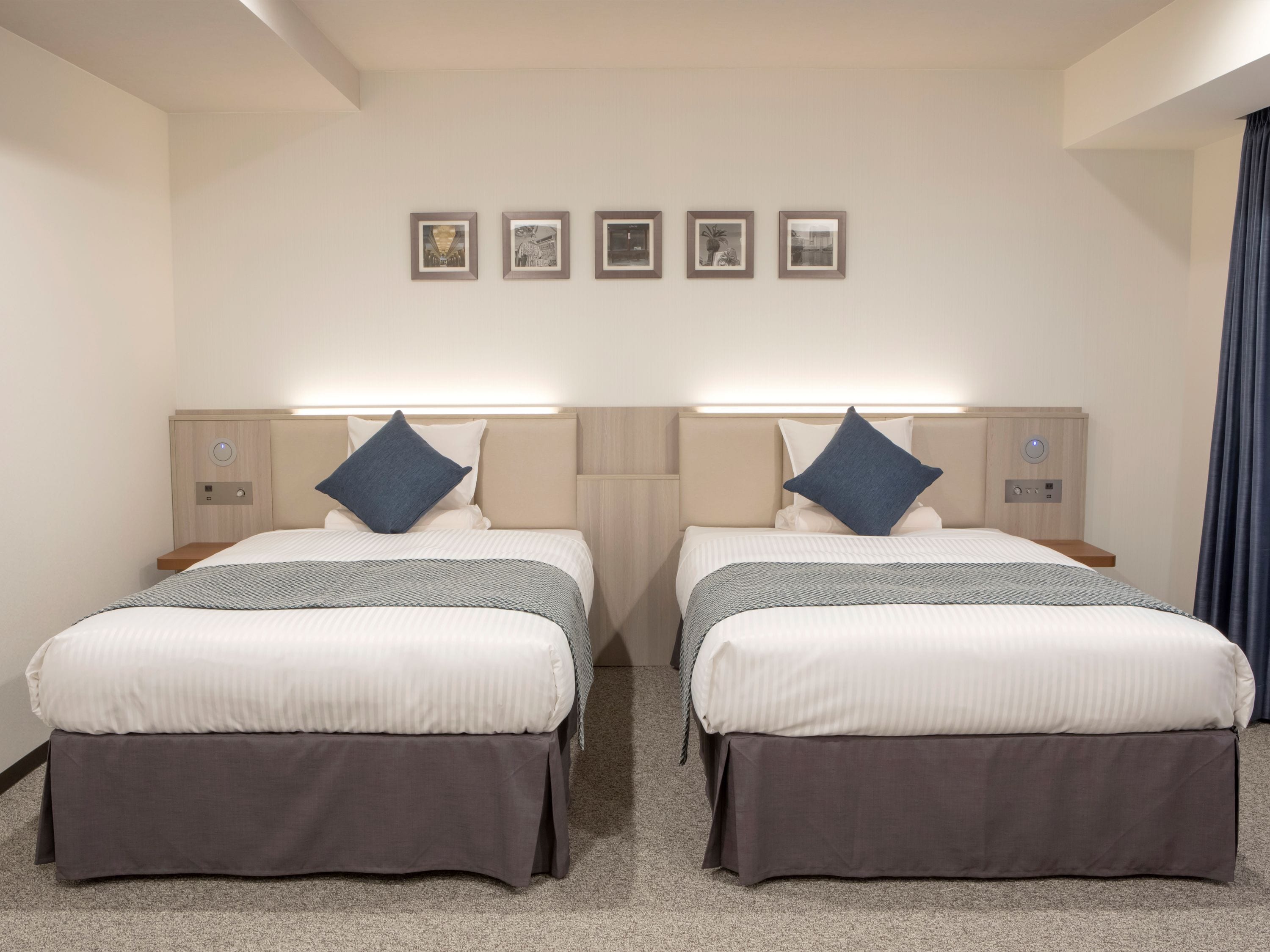 A hotel room with two beds, each with a headboard, bedside tables, and a flat-screen TV.