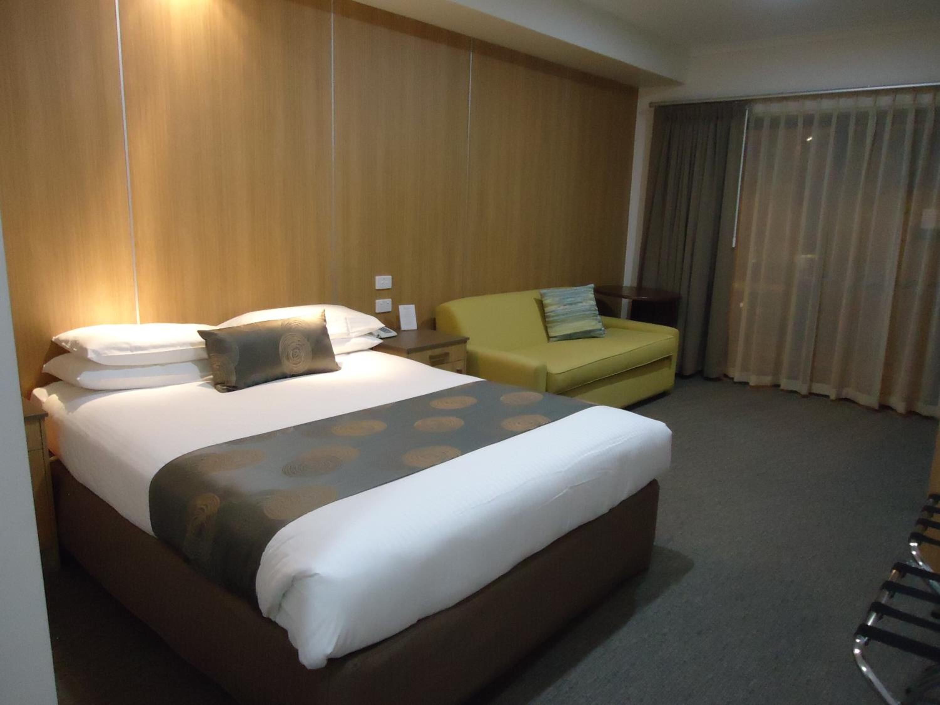 A hotel room with a large bed, a small sofa, a desk, and a window with curtains.