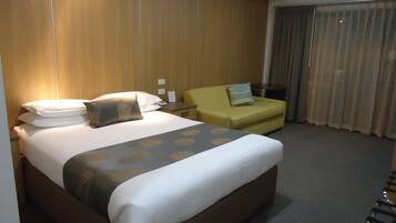 A hotel room with a large bed, a small sofa, a desk, and a window with curtains.