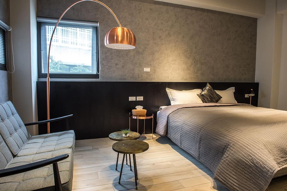 A modern bedroom with a bed, a chair, a table, and a floor lamp.