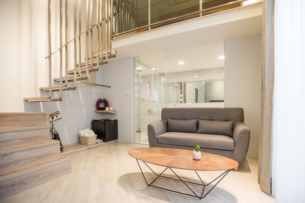 A modern living room with a grey sofa, a wooden coffee table, and a staircase with a minimalist design.